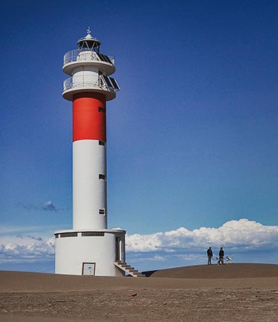 Attracties Foto van de vuurtoren van Fangar in het noorden van de Ebro-delta met een blauwe lucht, wolken aan de horizon en zand