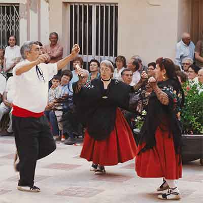 Home Foto van een oudere man en twee oudere dames die de Jota dansen in Benifallet tijdens de Fiesta Major