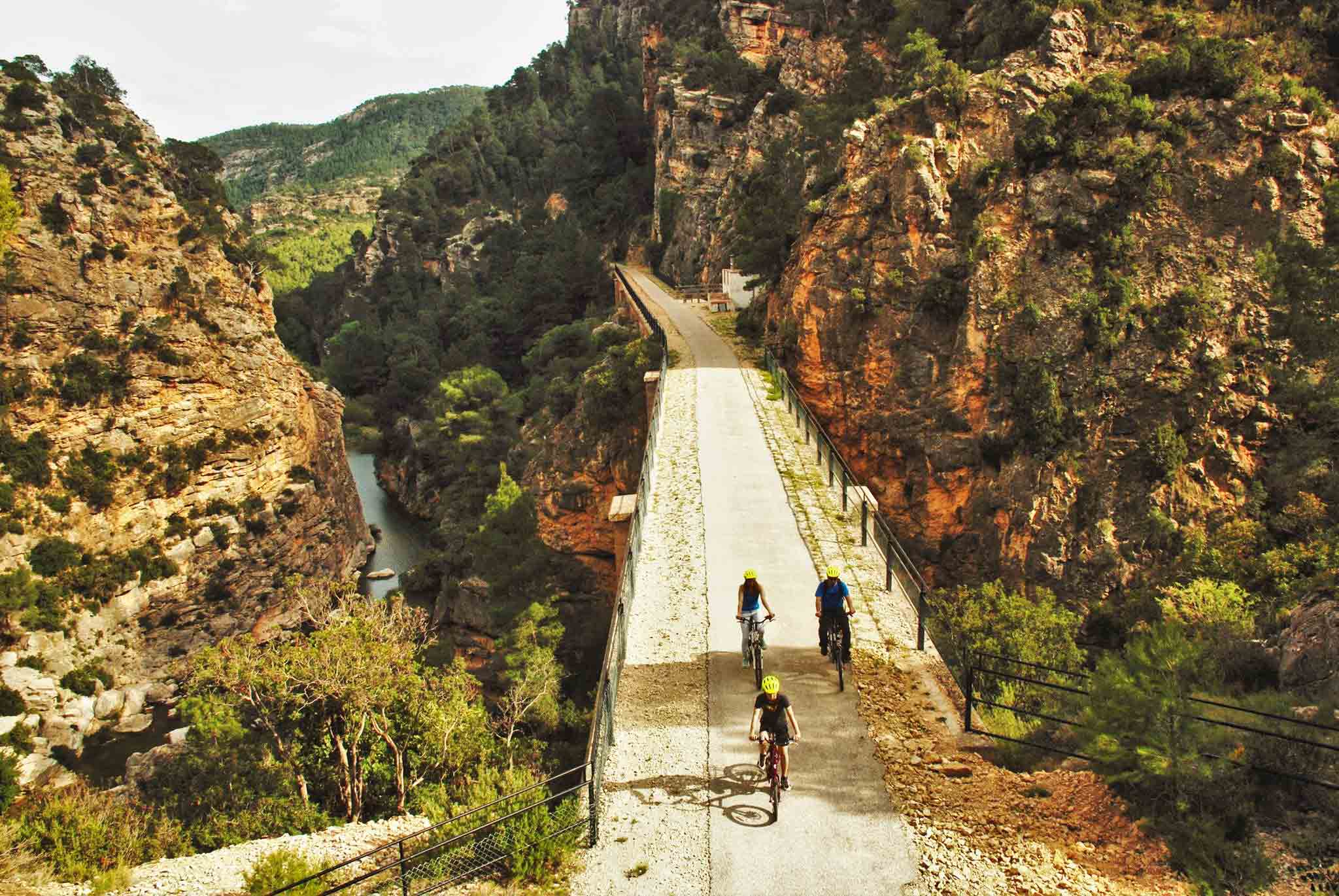 Home Drie mensen met gele helmen fietsen de Via Verde af met uitzicht op Font Calda en het Catalonië-gebergte