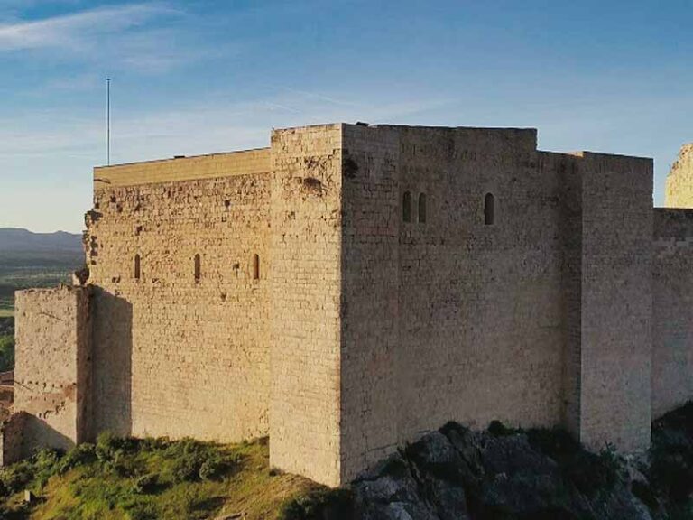 Photo of the medieval castle of Miravet which overlooks the Ebro River and surrounding mountains under a blue sky