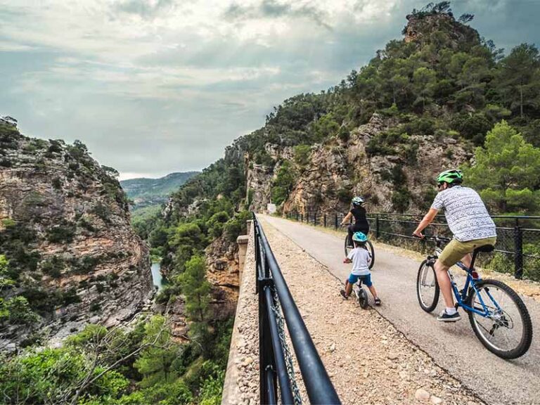 Photo of a family with a small child on bicycles crossing a bridge over the Via Verde near Xerta